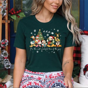May include: Dark green t-shirt featuring a festive graphic of Disney characters, including Mickey and Minnie Mouse, Donald Duck, and Goofy, in Christmas attire. The text "It's the most wonderful time of the year" is printed below the characters.