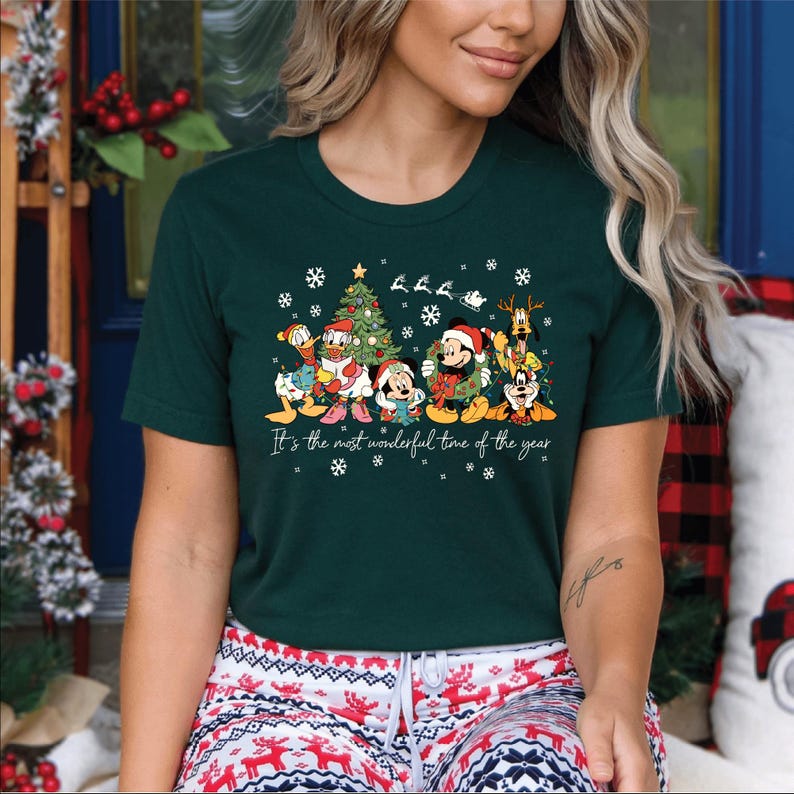 May include: Dark green t-shirt featuring a festive graphic of Disney characters, including Mickey and Minnie Mouse, Donald Duck, and Goofy, in Christmas attire. The text "It's the most wonderful time of the year" is printed below the characters.