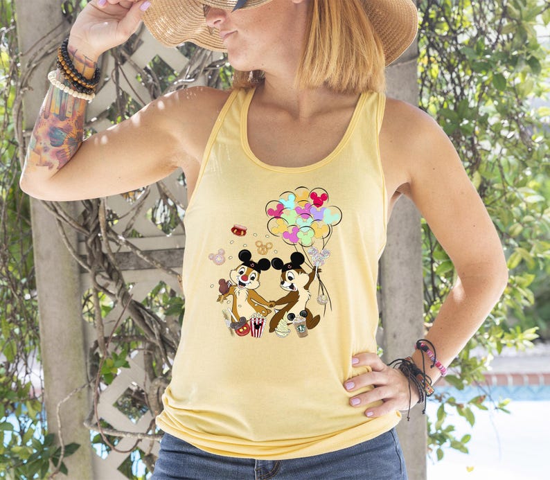 May include: A light yellow tank top featuring a cartoon graphic of Chip and Dale holding balloons. The graphic includes colorful balloons and popcorn. The tank top is sleeveless and has a rounded neckline.