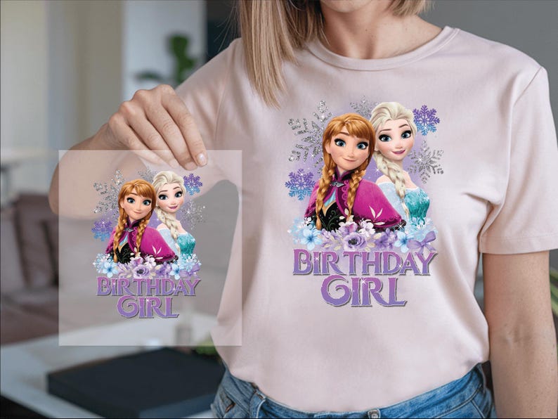 K&ouml;nnte beinhalten: Hellrosa T-Shirt mit einem Aufdruck von zwei animierten M&auml;dchen und dem Text "BIRTHDAY GIRL" in Lila. Die Grafik enth&auml;lt lila und blaue Blumenelemente und Schneeflocken.