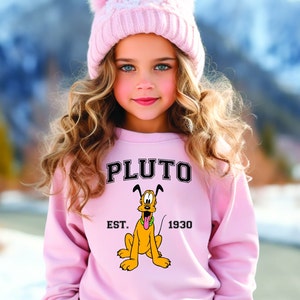 Puede incluir: Una sudadera rosa con una imagen de dibujos animados de Pluto, el perro de Disney, y el texto "PLUTO EST. 1930".