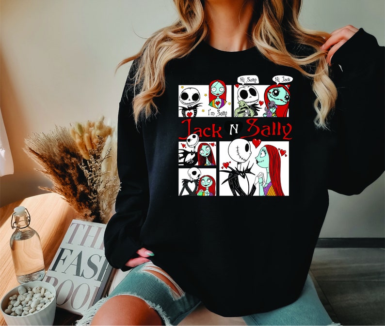 Puede incluir: Sudadera negra con un dise&ntilde;o de Jack y Sally de Pesadilla antes de Navidad. El dise&ntilde;o incluye varios paneles con los personajes y el texto "Jack N Sally" en rojo. La sudadera es de cuello redondo.