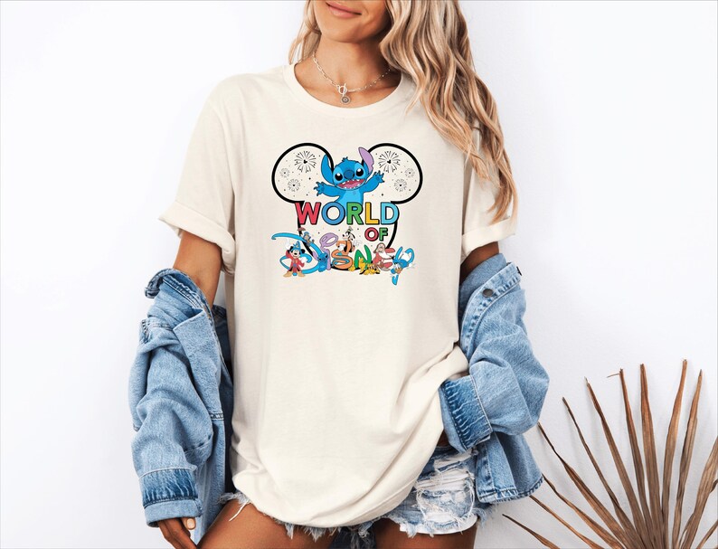 Pu&ograve; includere: T-shirt color crema con grafica colorata di Stitch di Lilo & Stitch, fuochi d'artificio e la scritta "WORLD OF DISNEY" in un font giocoso. Il design &egrave; racchiuso in un contorno di orecchie di Topolino. Parte di una collezione a tema Disney.