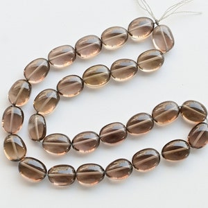 May include: A strand of oval-shaped smoky quartz beads. The beads are translucent and have a light brown color.