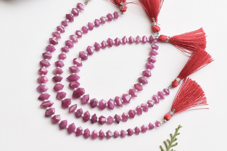 Pu&ograve; includere: Tre fili di perline di rubino rosa con superfici sfaccettate. Le perline sono infilate su un filo d'argento e hanno nappine rosse alle estremit&agrave;.