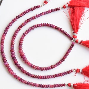 Op de afbeelding: Drie strengen roze robijn edelsteen kralen met rode kwastjes. De strengen zijn van verschillende lengtes.