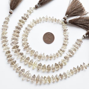 May include: Three strands of light brown faceted gemstone beads with brown tassels. The beads are arranged in a circle around a US penny for size reference.