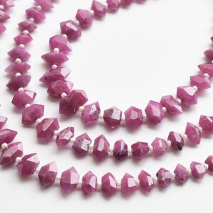 Pu&ograve; includere: Una collana di perle di pietre preziose rosa con una forma sfaccettata, simile a un diamante. Le perle sono infilate su un filo bianco e sono separate da piccole perle bianche.