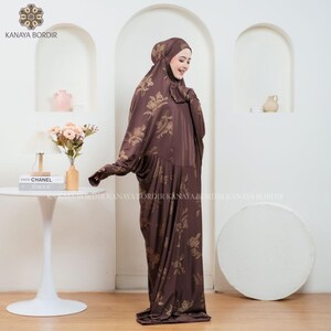 Może przedstawiać: Brązowa szata modlitewna z kwiatowym wzorem. Str&oacute;j zawiera nakrycie głowy i luźny, długi kr&oacute;j. Nazwa marki "KANAYA BORDIR" jest widoczna w lewym g&oacute;rnym i dolnym rogu zdjęcia.
