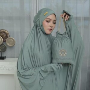 Może przedstawiać: Zestaw do modlitwy w kolorze szałwii, w tym nakrycie głowy i pasująca torba ze sznurkiem. Torba posiada haftowany wz&oacute;r i napis "KANAYA BORDIR". Zestaw wykonany jest z miękkiej, zwiewnej tkaniny.