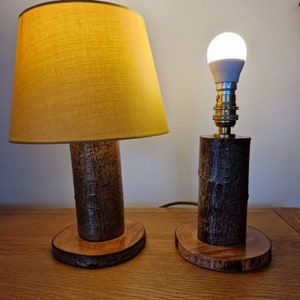 May include: Two wooden table lamps with natural bark bases and round wooden tops. The lamp on the left has a yellow fabric lampshade. The lamp on the right has a white light bulb.