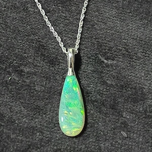 May include: A teardrop-shaped opal pendant featuring vibrant flashes of green and yellow, set in a polished silver-toned metal bail and suspended from a delicate silver-toned rope chain necklace that catches the light with its intricate texture.