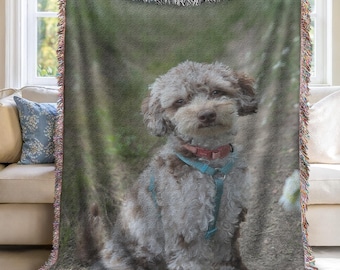 May include: Woven throw blanket featuring a portrait of a dog with gray and brown fur, wearing a red collar and blue harness. The blanket has a fringed edge and is held up by two people in front of a window.