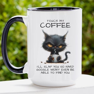 May include: White ceramic coffee mug with a black handle and rim. The mug features a grumpy black cat illustration holding a coffee cup, with the text "TOUCH MY COFFEE" and "I'LL SLAP YOU SO HARD GOOGLE WON'T EVEN BE ABLE TO FIND YOU."
