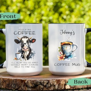 May include: White ceramic coffee mug with a black handle. The front of the mug features a cartoon cow wearing glasses and holding a cup of coffee. The text "Touch My Coffee" is above the cow and the text "I'll slap you so hard Google won't even be able to find you" is below the cow. The back of the mug features a watercolor illustration of a cup of coffee with flowers and the text "Johnny's Coffee Mug".