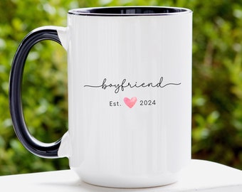 May include: White ceramic mug with a black handle. The mug has the text "boyfriend" with a pink heart and "Est. 2024" printed on it.