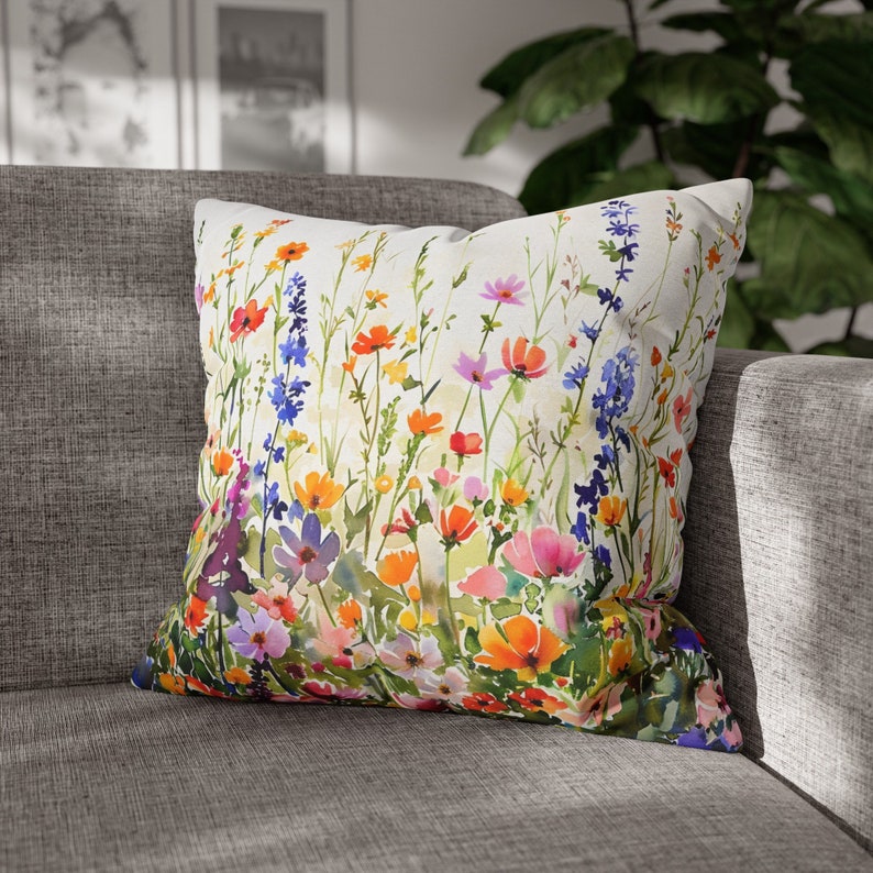 May include: A white throw pillow with a watercolor floral print featuring a variety of colorful flowers, including pink, orange, yellow, blue, and purple.