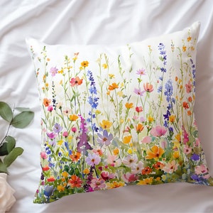 May include: A white pillow with a watercolor print of a field of colorful wildflowers. The flowers are in shades of pink, purple, yellow, orange, and blue.
