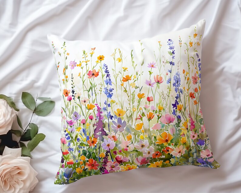 May include: A white pillow with a watercolor print of a field of colorful wildflowers. The flowers are in shades of pink, purple, yellow, orange, and blue.