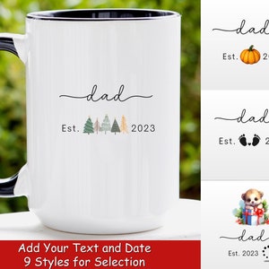 May include: White ceramic mug with a black rim and handle. The mug has a design that says "dad est. 2023" with a row of small Christmas trees. The text is in a handwritten font.