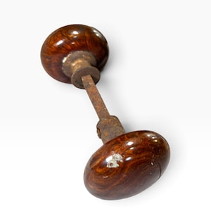 May include: A vintage door knob set featuring two round, polished brown marbled knobs connected by a central square metal spindle. The hardware exhibits a dark, weathered patina on the connecting rod and base components, contrasting with the smooth, glossy, swirling brown and amber patterns of the spherical knobs.