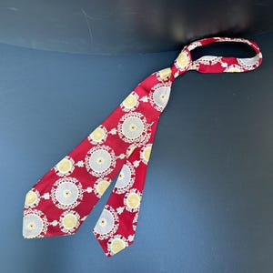 May include: A red silk tie with a white and yellow geometric pattern. The tie has a pointed end and a narrow width.