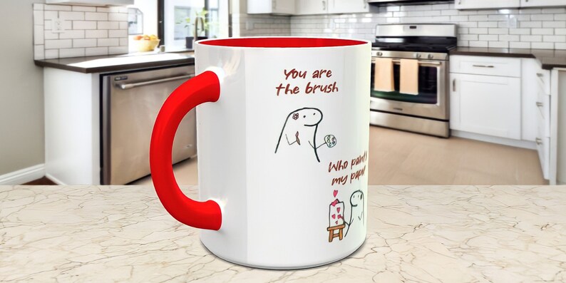 May include: White ceramic mug with a red handle and red rim. The mug has a black and white illustration of a person holding a paintbrush and a canvas. The text on the mug reads "You are the brush. Who paints my paper?"