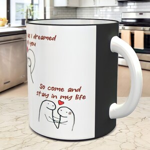 May include: White ceramic mug with a black rim and handle. The mug has a red and black illustration of two stick figures with a heart and the text "So come and stay in my life".