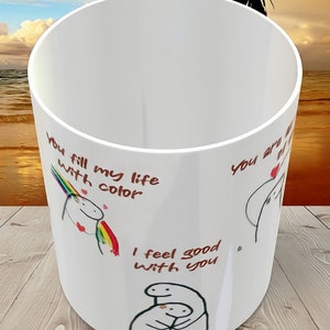 May include: White ceramic mug with a red and black illustration of a unicorn and the text "You fill my life with color". The mug also has the text "I feel good with you" and a black and white illustration of two people hugging.