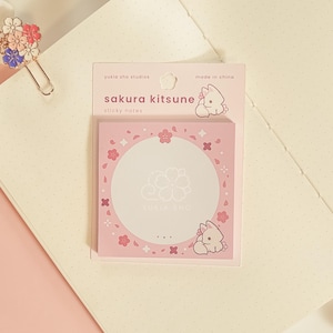 May include: Pink Sakura Kitsune sticky notes with a floral design. The notes feature a central circle with a flower graphic and the text "yukia sho studios". The packaging includes a cartoon fox illustration and the text "sakura kitsune".