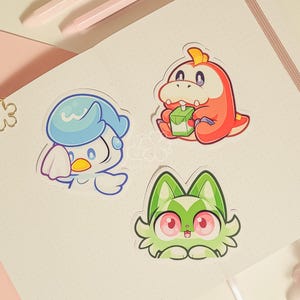 May include: Three cartoon character stickers on a white background. The stickers are of a blue bird, a green cat, and a red dinosaur holding a carton of milk.