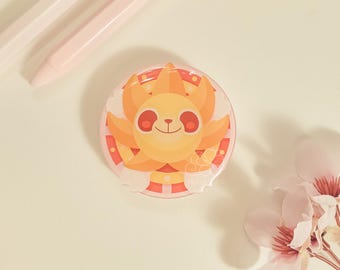 May include: A round, colorful button featuring a cartoon sun with a smiling face. The sun has orange and yellow rays. The button is on a light background with pink pens and flowers.