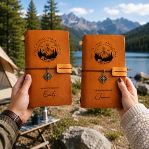 May include: Two tan leather journals with elastic closures and metal compass charms. Each cover features a circular mountain landscape graphic with the text "EMILY & JAMES TRAVEL JOURNAL" and "THE ADVENTURES OF EMILY" or "THE ADVENTURES OF JAMES".