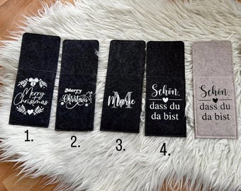 Könnte beinhalten: Eine Auswahl an Handyhüllen aus Filz in Schwarz und Grau. Die Hüllen zeigen weiße Schriftzüge und Designs, darunter "Merry Christmas", einen einzelnen Buchstaben und den Satz "Schön, dass du da bist".
