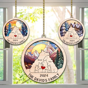 May include: Three wooden Christmas baubles featuring a mountain scene, a winter cabin scene, and a sunset scene. Each bauble depicts a family of bears with personalised names and the year 2024. The text "The David's Family" is on each bauble.