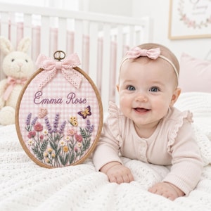 May include: An oval wooden embroidery hoop featuring a light pink and white gingham fabric background. The embroidery displays the name Emma Rose in cursive script above a colorful floral arrangement with lavender, daisies, and two butterflies.