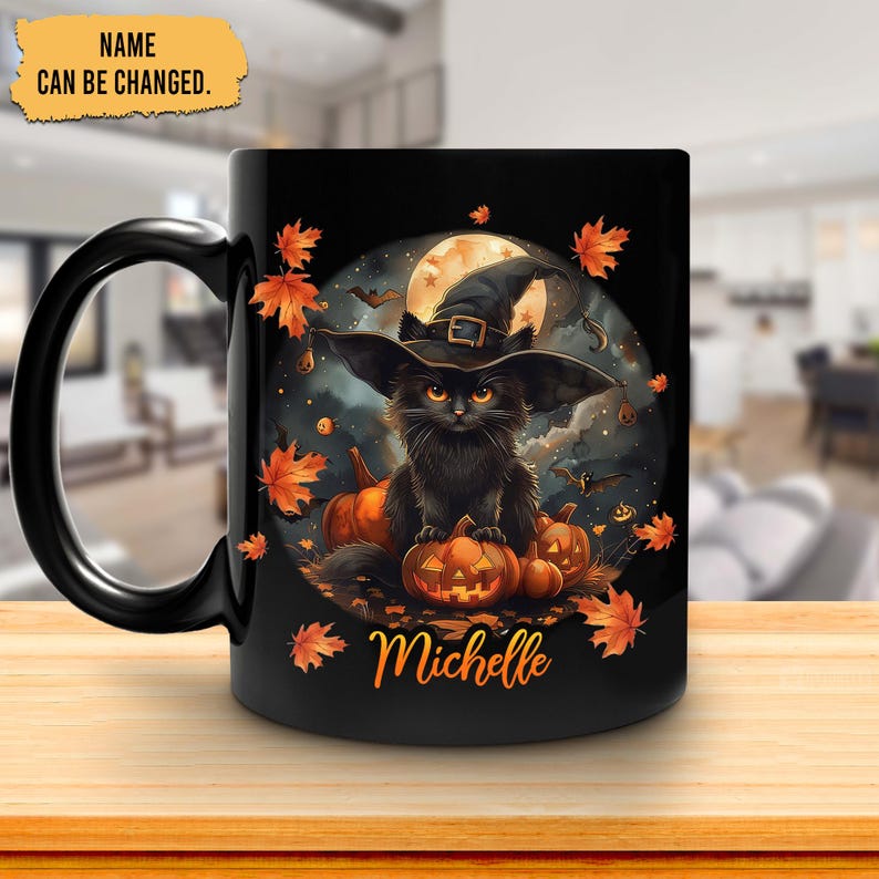 Op de afbeelding: Zwarte keramische mok met een Halloween-ontwerp. Het ontwerp bevat een zwarte kat met een heksenhoed, pompoenen en herfstbladeren. De naam "Michelle" is in oranje letters op de mok gedrukt.