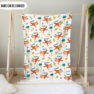 May include: A white baby blanket with a repeating pattern of brown monkeys swinging from palm trees. The monkeys are smiling and have yellow eyes. The background is white with green leaves, yellow flowers, and orange and yellow rainbows. The text "DAVID" is repeated throughout the blanket.