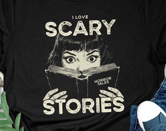 May include: Black t-shirt with a graphic of a woman reading a book with the text "I love scary stories" on it.