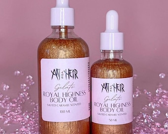 May include: Two glass bottles of body oil with white droppers. The bottles are filled with a shimmering, golden liquid. The labels read "ANHEIR Gelato ROYAL HIGHNESS BODY OIL SALTED CARAMEL SCENTED" with sizes 100 ml and 50 ml.