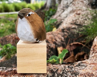 May include: A small wooden bird figurine with brown and white paint, perched on a wooden block.