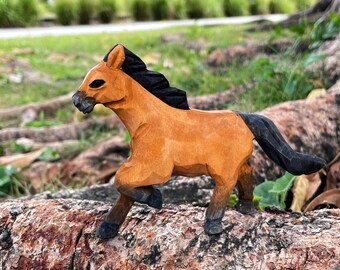 Könnte beinhalten: Eine Holzpferdefigur mit braunem Körper und schwarzer Mähne und Schwanz. Das Pferd steht auf einem Baumstamm.