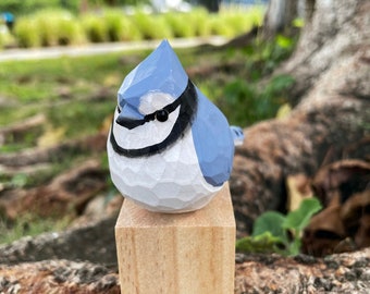 May include: A small, hand-carved wooden bluebird figurine with a white chest and black eye detail. The bird is perched on a small wooden block.