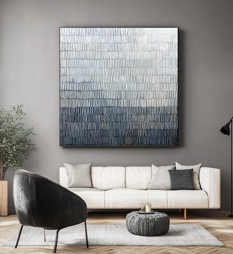 May include: Large abstract wall art in shades of blue, grey, and white. The artwork features a textured, layered design with vertical brushstrokes. The piece is framed in black and hangs above a white sofa in a modern living room.
