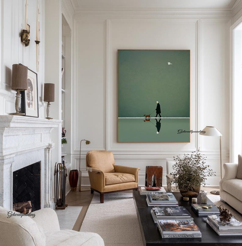 May include: A framed art print depicts a person walking a dog on a white line against a green background. The artwork has a minimalist style, with a reflection of the person and dog below. The room features a fireplace, armchair, and coffee table.