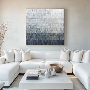 May include: A contemporary living room with an abstract artwork in shades of white, grey, and navy blue. A white corner sofa, a white square coffee table, and decorative items such as vases and a wooden bowl are also visible.
