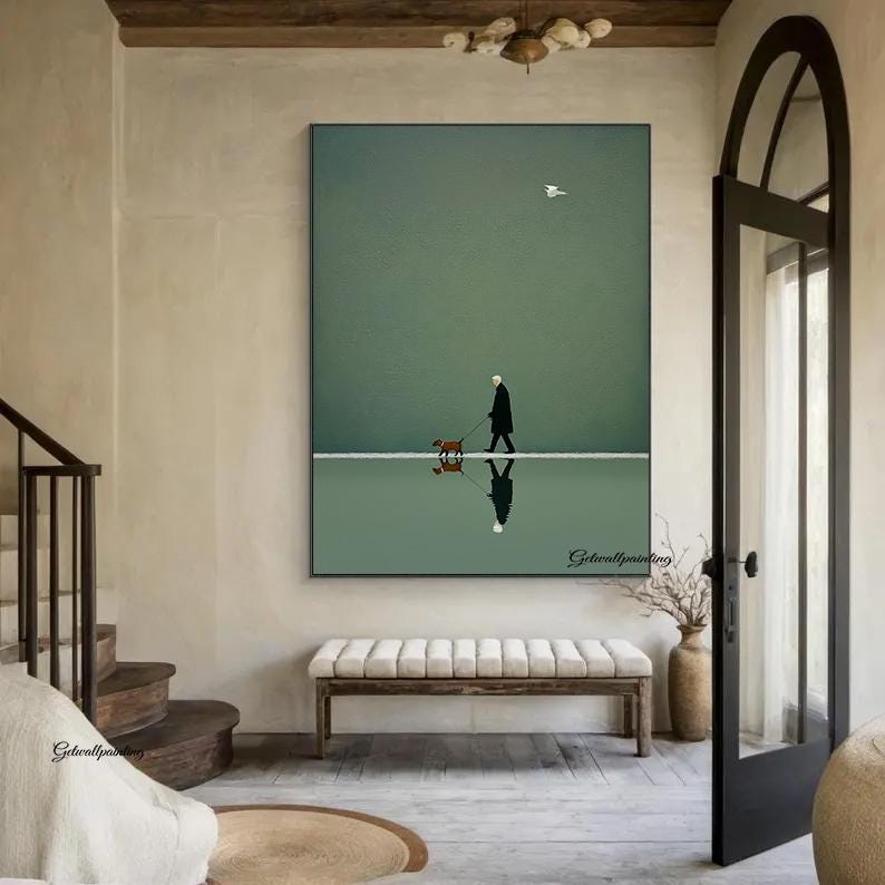 May include: A framed art print depicts a person walking a dog on a reflective surface, with a seagull in the sky. The artwork features a minimalist style with a muted color palette of green, white, and brown. The print is displayed in a room with a bench and a staircase.