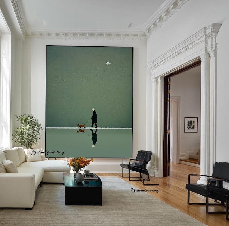 May include: A large framed art print depicts a person walking a dog on a reflective surface, with a bird in the sky. The artwork is set against a muted green background, creating a serene and minimalist aesthetic. The scene is reflected in the water.