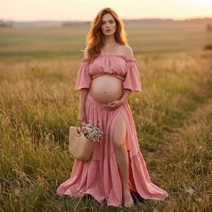 May include: A two-piece maternity set consisting of a dusty pink off-the-shoulder crop top with ruffled sleeves and a matching high-waisted maxi skirt featuring a high side slit. A woven straw handbag filled with small white flowers is held.