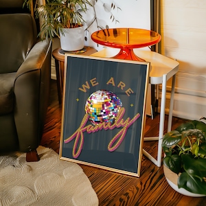 May include: A gold framed poster with a dark blue background featuring a disco ball and the text "We Are Family" in pink with yellow light bulbs around the text.